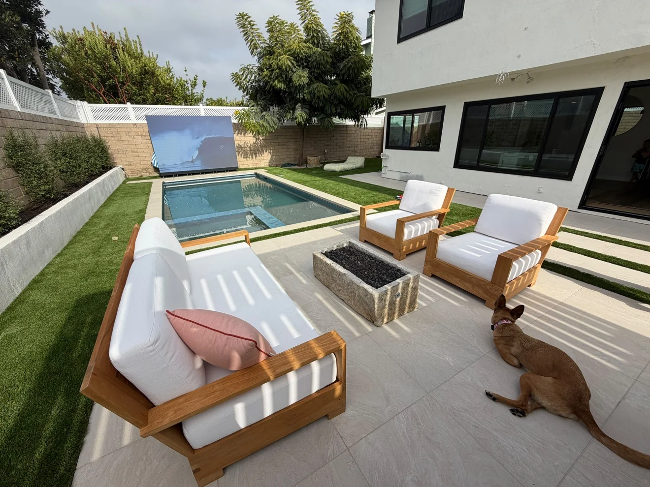 Poolside lounge with backyard theater by Moda Outdoor Living in Huntington Beach, CA — luxury outdoor living design and build