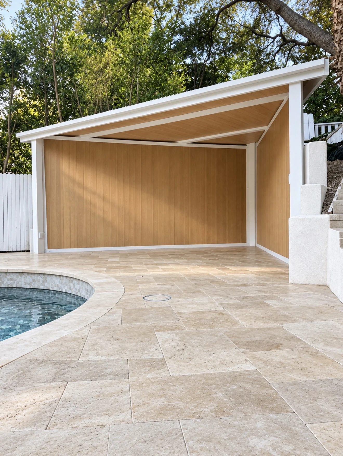 Wood-paneled patio cover over travertine pool deck by Moda Outdoor Living in Brentwood, CA — luxury outdoor living design and build