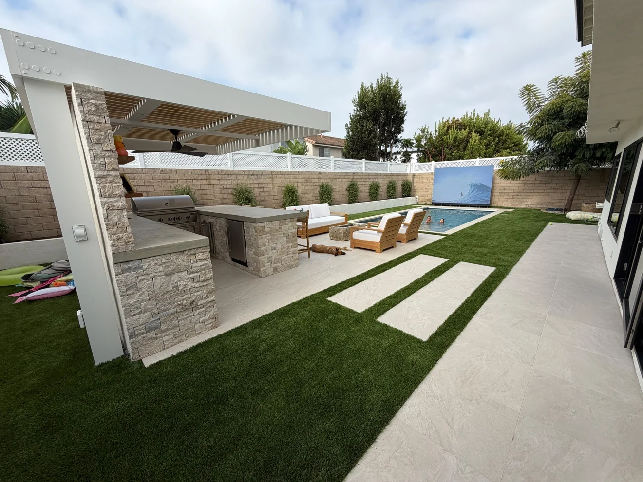 Backyard theater and pool with turf lawn by Moda Outdoor Living in Huntington Beach, CA — luxury outdoor living design and build