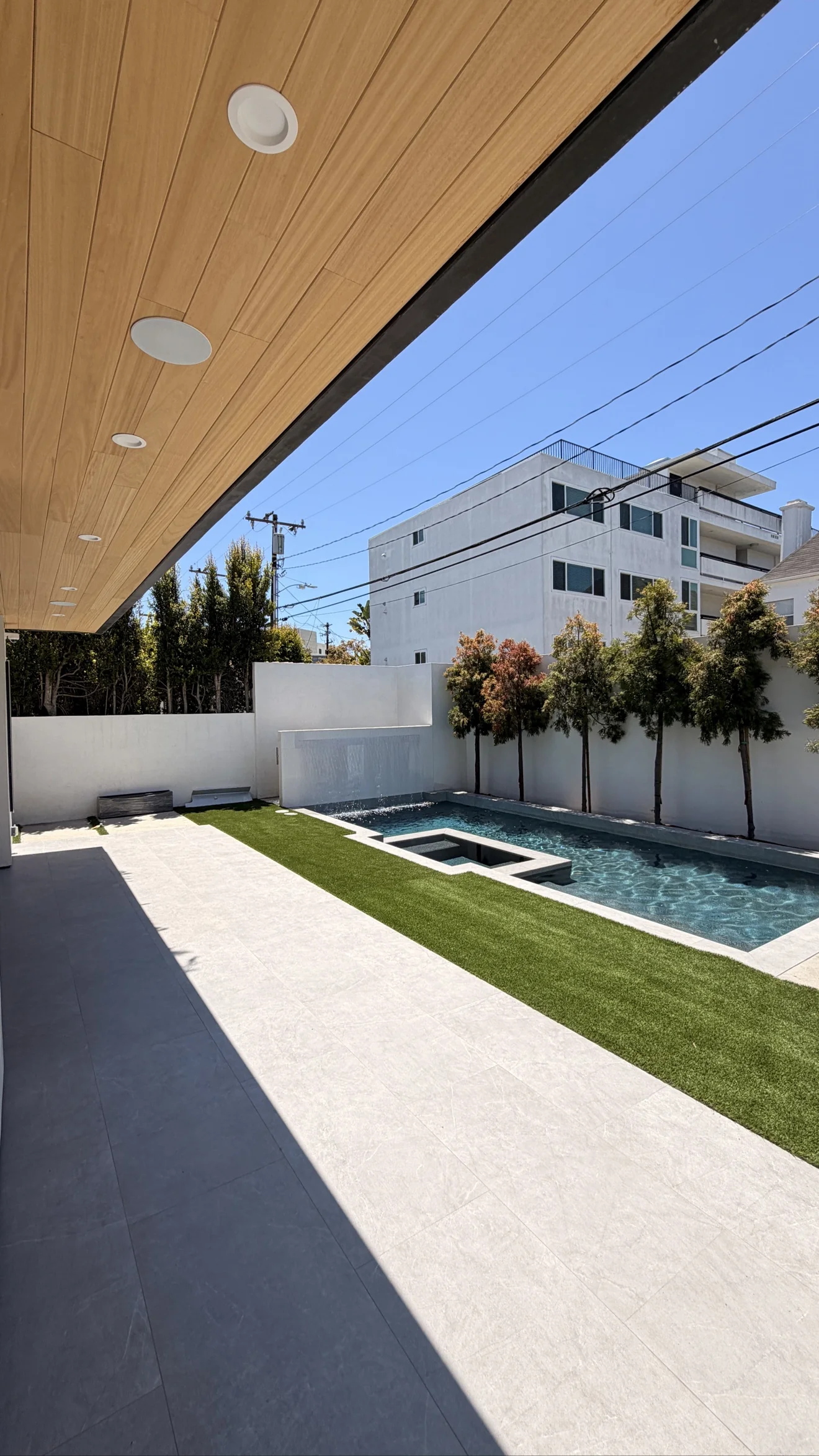 Covered patio with wood ceiling and pool by Moda Outdoor Living in Beverly Hills, CA — luxury outdoor living design and build