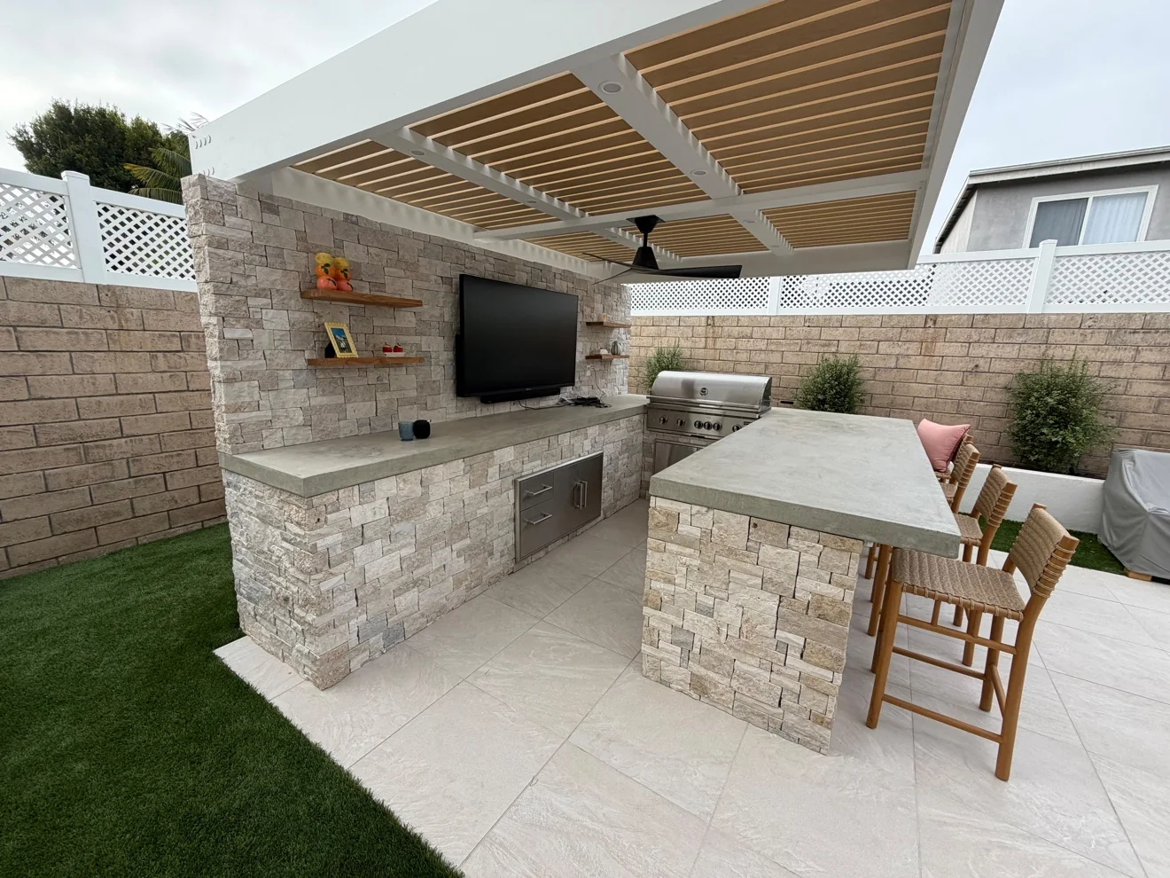 Stone outdoor kitchen with TV and bar seating by Moda Outdoor Living in Huntington Beach, CA — luxury outdoor living design and build