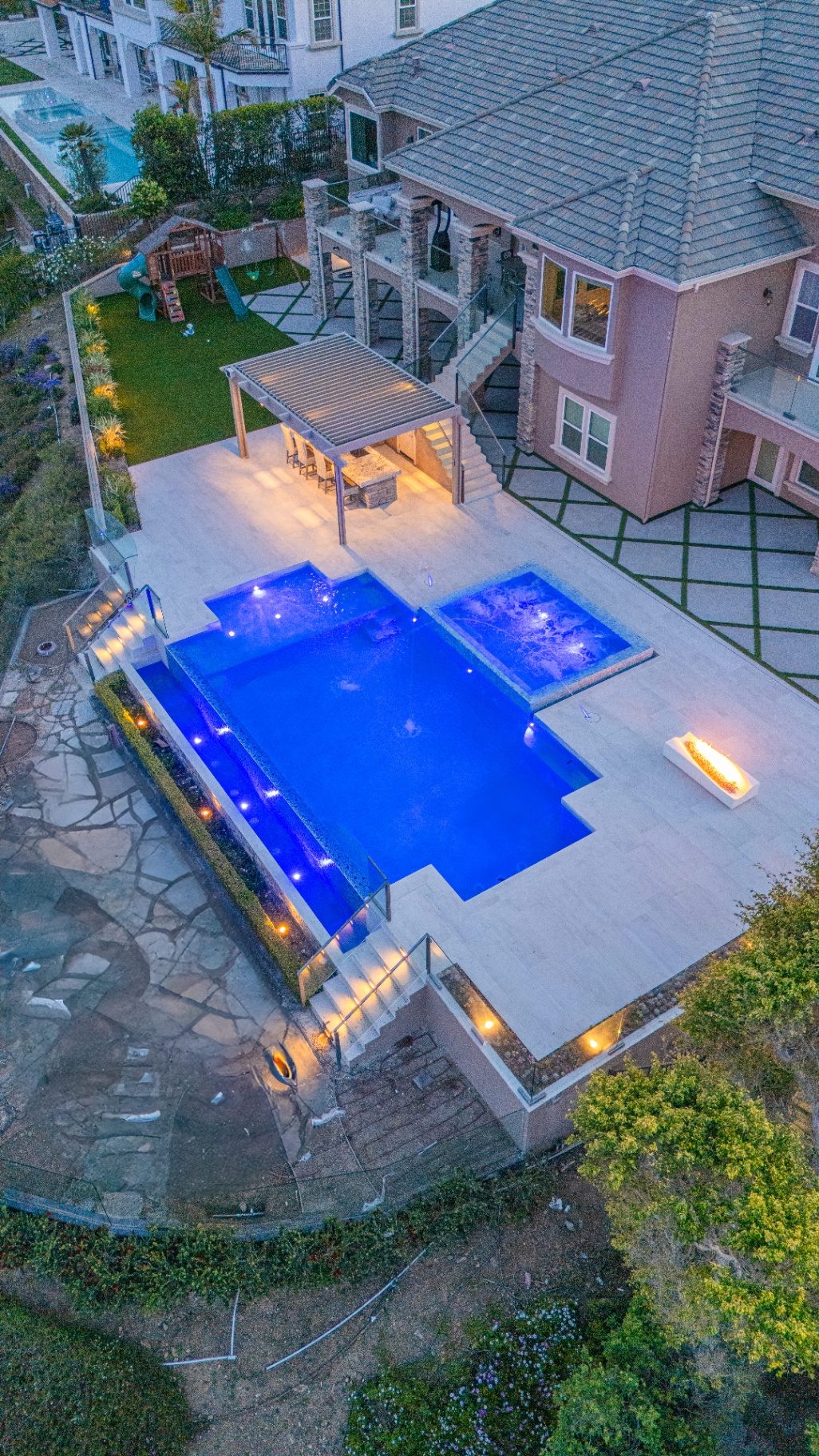Professionally lit backyard with pool, landscape lighting, and pergola at night in Los Angeles