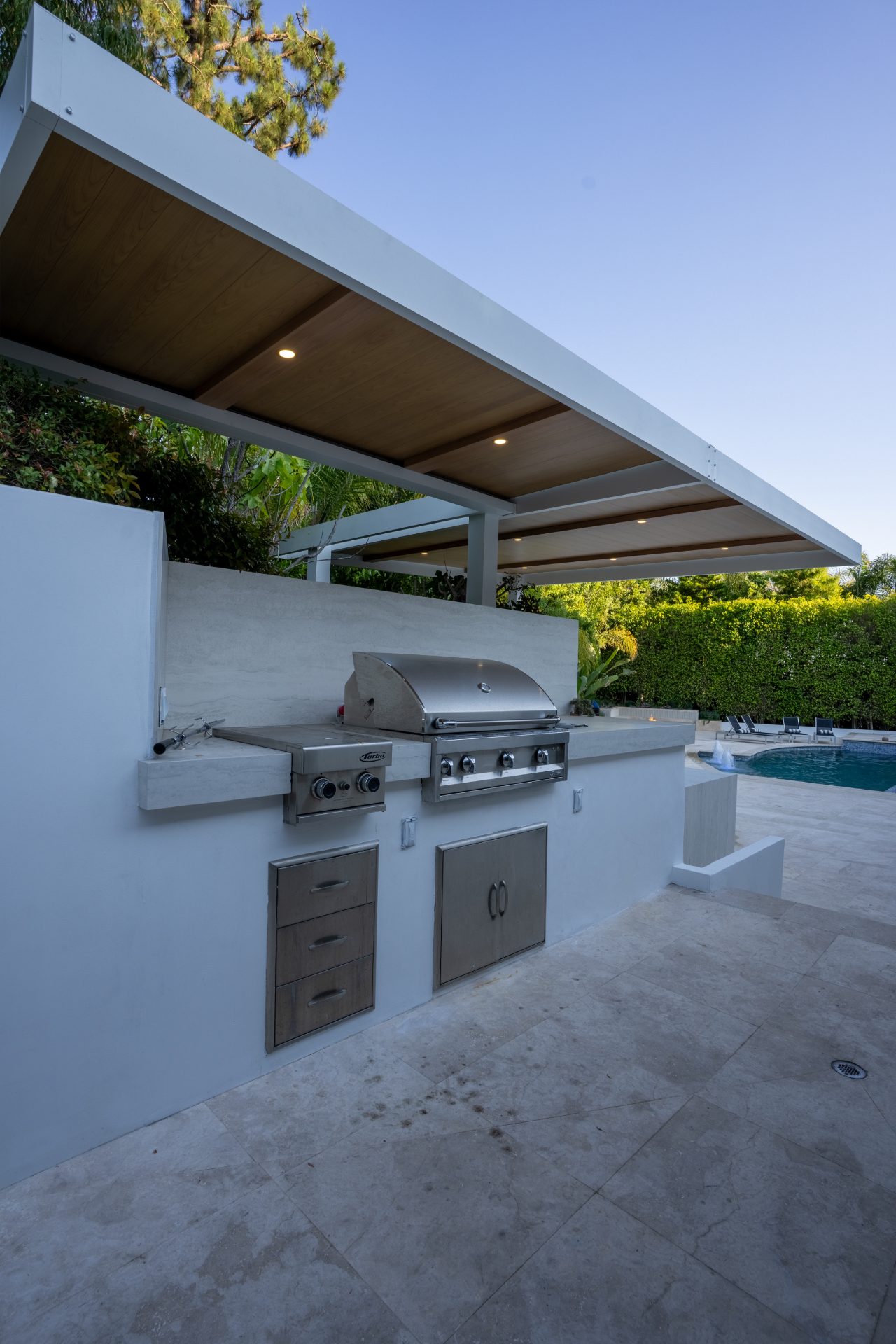 BBQ grill station under pergola with pool in background