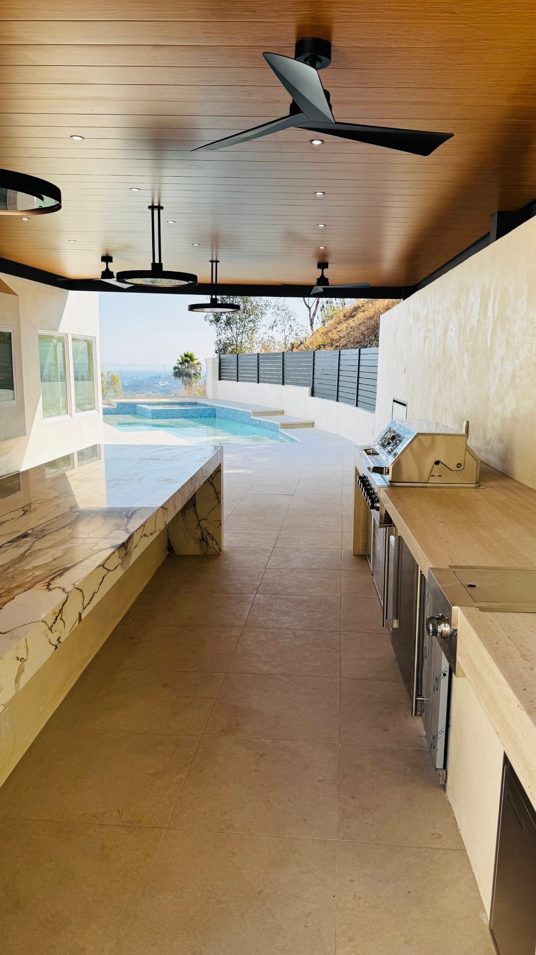 Covered outdoor kitchen with bar seating and pool view