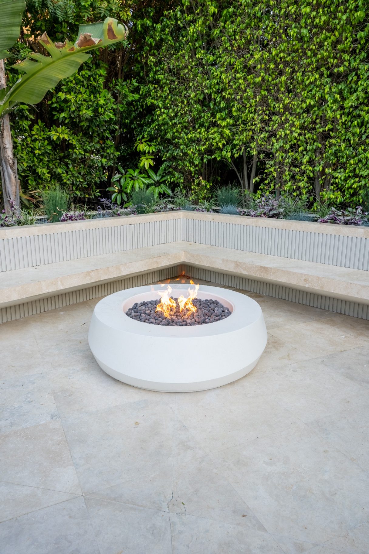 Custom fire pit with travertine bench seating on a paver patio in Los Angeles
